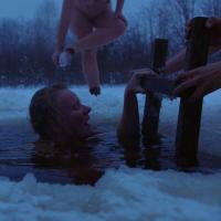 Nude women climbing out of water after swimming in snow-covered lake.