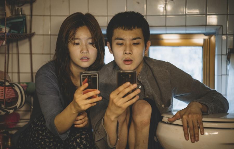 A girl and a boy sit very close together looking at their phones.