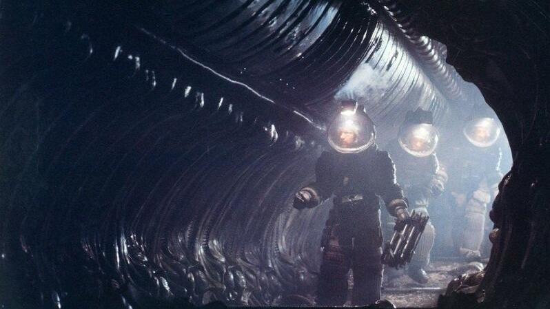 Three figures in space suits walking through a shadowy tunnel