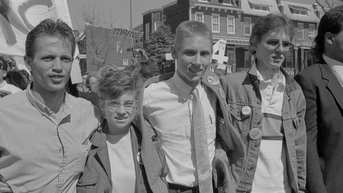 A black-and-white photograph of four students marching arm-in-arm at a protest.
